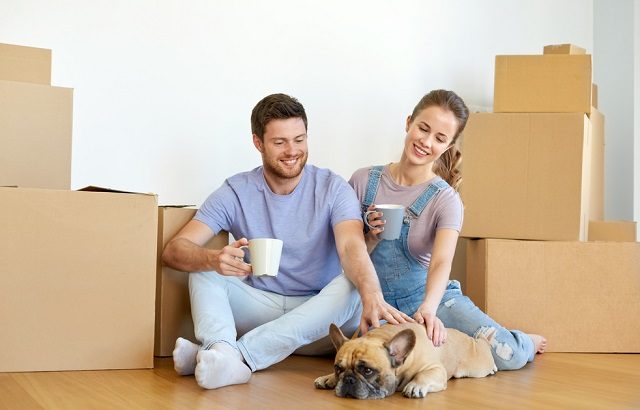 happy couple with boxes and dog moving to new home